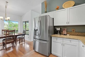 Una cocina moderna con armarios blancos, un refrigerador de acero inoxidable y un comedor con sillas y mesa de madera.