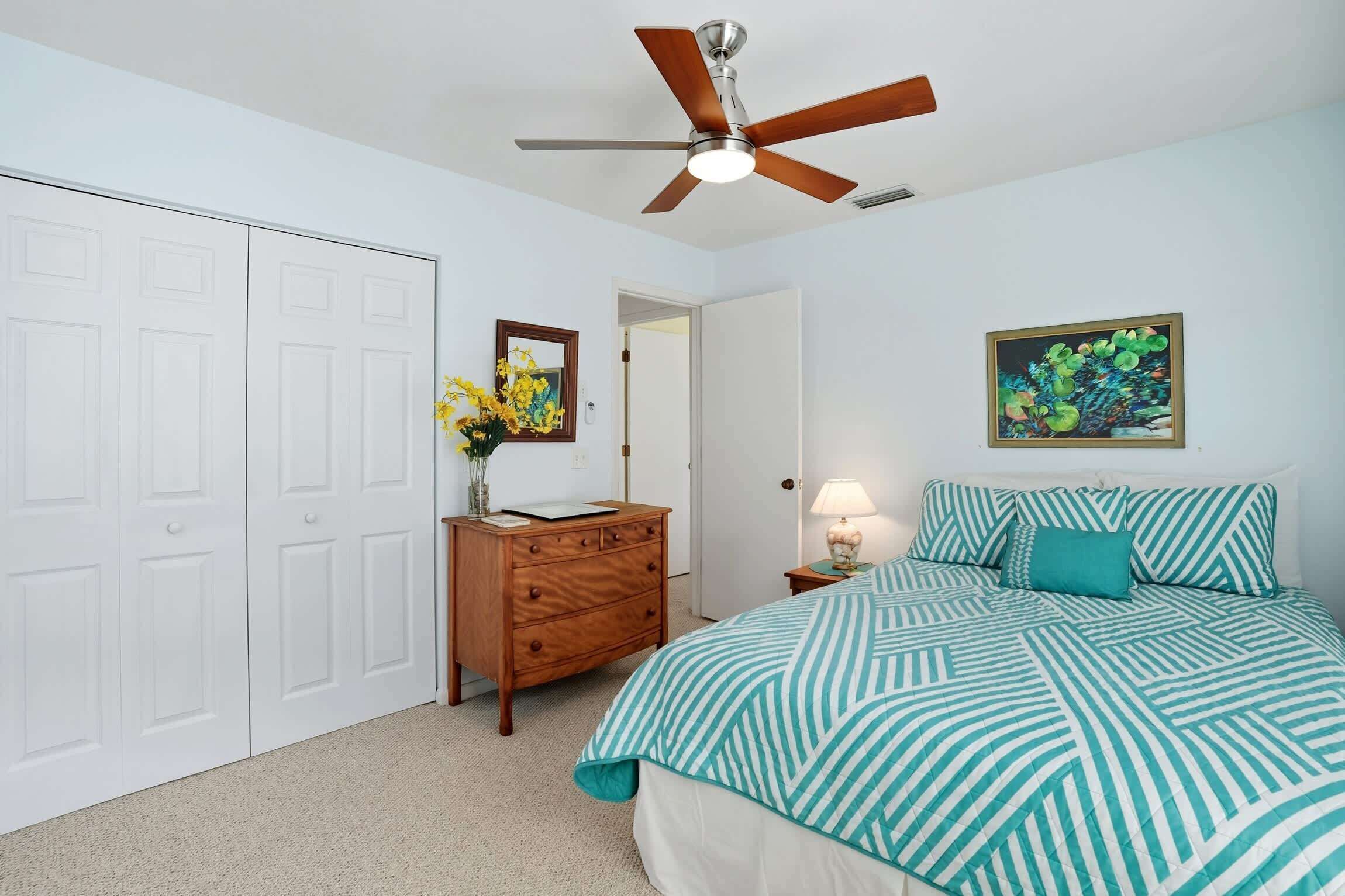 A bedroom with a bed, a dresser, a ceiling fan, a door, and a framed picture on the wall.