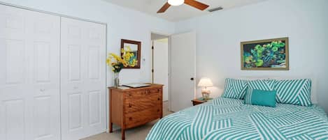 A bedroom with a bed, a dresser, a ceiling fan, a door, and a framed picture on the wall.