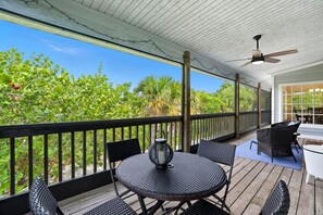 Eine überdachte Terrasse im Freien mit einem runden Tisch und Stühlen, einem Deckenventilator und Blick auf üppiges Grün.