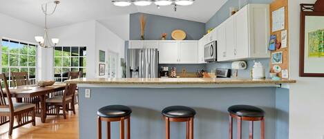 A modern kitchen with white cabinets, a stainless steel refrigerator, and a bar area with stools.