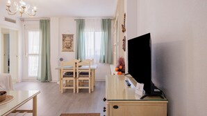 A living room with a television, a dining table with chairs, a chandelier, and a window with curtains. - Stunning Views of Seville (San Juan de Aznalfarache)