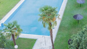 A rectangular swimming pool with a clear blue water surface, surrounded by a well-maintained lawn and palm trees. - Stunning Views of Seville (San Juan de Aznalfarache)