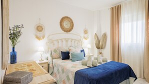 A bedroom with a bed, bedside tables, a lamp, a vase with flowers, and a decorative headboard. - Stunning Views of Seville (San Juan de Aznalfarache)