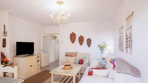 A living room with a TV, a chandelier, a sofa, a coffee table, and decorative wall art. - Stunning Views of Seville (San Juan de Aznalfarache)