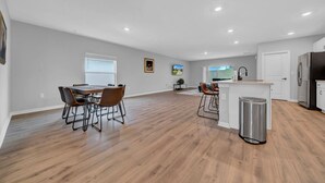 A spacious kitchen with a central island, a dining area with a long table and chairs, and a view of the outdoors through large windows.