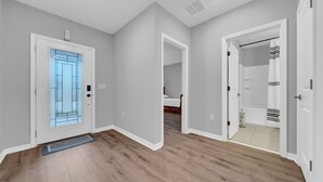 A hallway with wooden flooring, a glass door with a metal frame, and a white door leading to a bathroom.