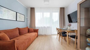 A living room with a sofa, dining table, chairs, a TV, and a window with curtains. - Spacious Apartment in the Center | Balcony and Air Conditioning (Wrocław)