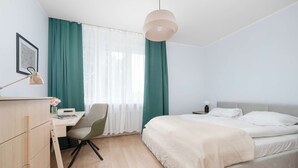 A modern bedroom with a bed, desk, chair, and a hanging light fixture. - Spacious Apartment in the Center | Balcony and Air Conditioning (Wrocław)