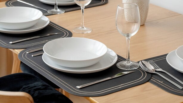 A dining table set with white plates, cutlery, and two wine glasses, accompanied by a vase of pink flowers. - Spacious Apartment in the Center | Balcony and Air Conditioning (Wrocław)