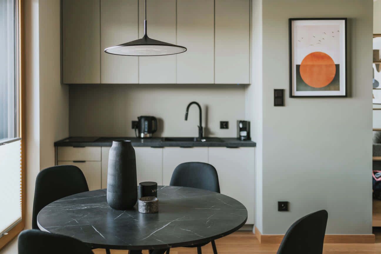 A modern kitchen with a round dining table, black chairs, and a pendant light.