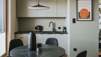 A modern kitchen with a round dining table, black chairs, and a pendant light.