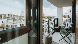 Ein Balkon mit Tisch und Stühlen, Blick auf die Stadtlandschaft und ein Fenster mit Ausblick auf Gebäude.