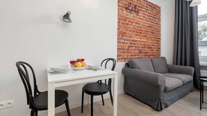 A modern living space with a white table, black chairs, a grey sofa, and a brick accent wall. - Cozy Apartment | Close to Manufaktura and Piotrkowska Street (Łódź)