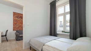 A bedroom with a bed, a desk, a chair, a brick wall, and a window with curtains. - Cozy Apartment | Close to Manufaktura and Piotrkowska Street (Łódź)