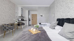 A modern, compact living space with a dining area, a bed with grey bedding, and a kitchen in the background. - Stylish Studio in the Center of Katowice | Balcony | Parking (Katowice)