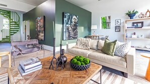 Un salon moderne avec un mur d’accent vert, un canapé, une table basse avec des livres et un bol décoratif, et un escalier en colimaçon en arrière-plan.