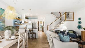 Un vaste espace de vie comprenant une table à manger, des chaises, un canapé, un escalier et, au fond, une cuisine.