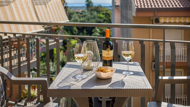 Un balcon avec une table dressée pour deux personnes, agrémentée d’une bouteille de vin, de deux verres et d’un bol de collations.