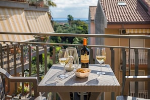A balcony with a table set for two, featuring a bottle of wine, two glasses, and a bowl of snacks. - Apartment 'Sicily Sweet Home' with Sea View, Wi-Fi and Air Conditioning (Fiumefreddo Sicilia)