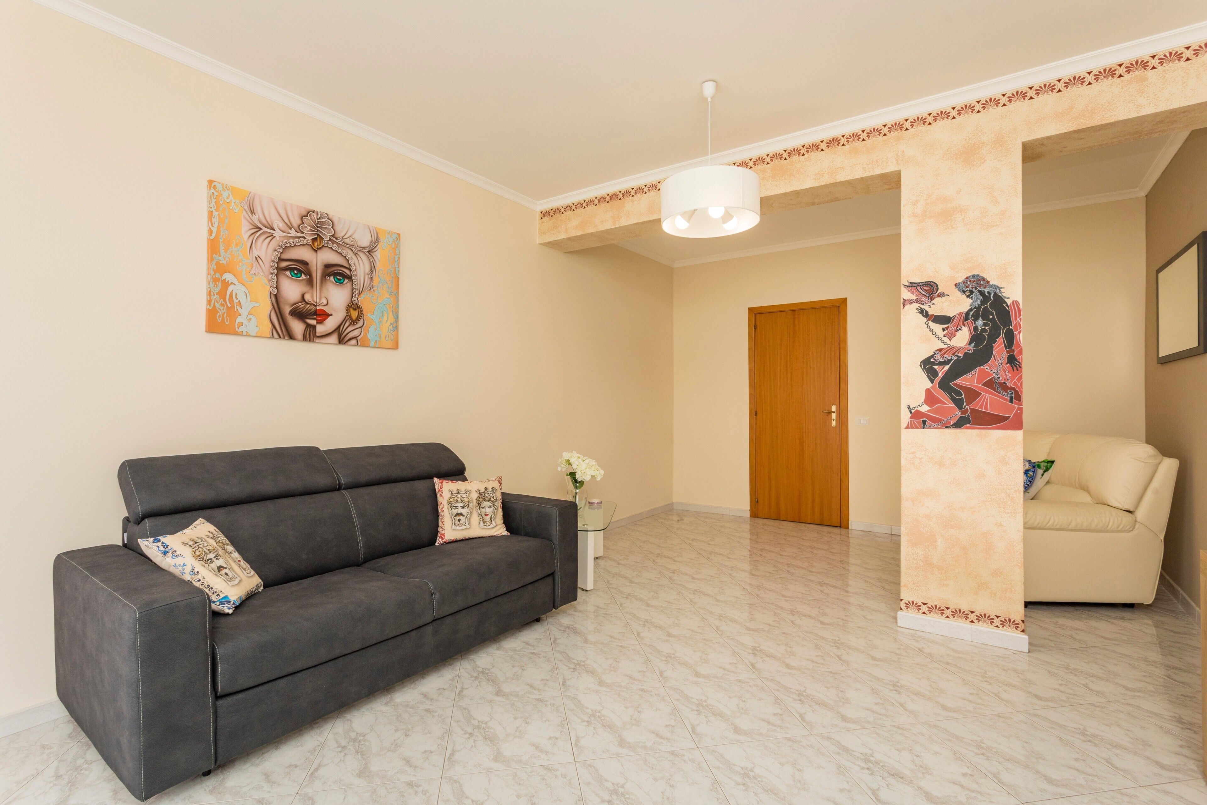 Ein modernes Wohnzimmer mit einer dunklen Couch, einem kleinen Beistelltisch mit einer Vase und einem großen abstrakten Gemälde an der Wand.