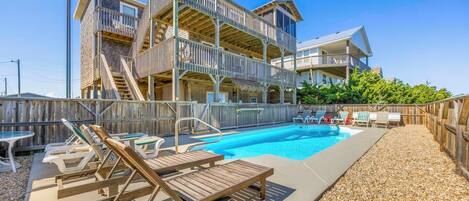 A multi-level building with a pool area, including lounge chairs and a staircase.