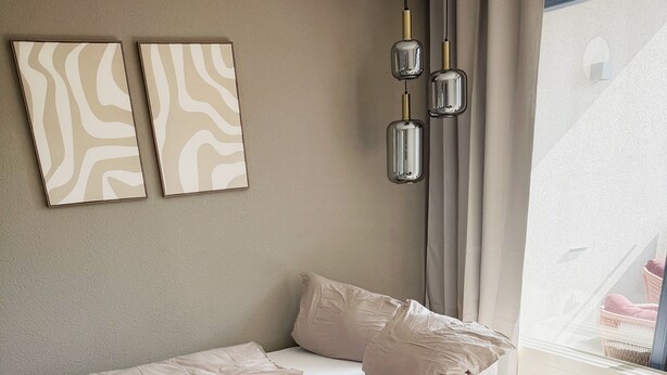 Quarto moderno com cama, travesseiros, cobertor, mesa de cabeceira com um copo e mesa redonda de madeira.
