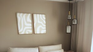 Uma sala de estar moderna com um sofá bege, duas mesas laterais redondas de madeira e arte abstrata na parede.