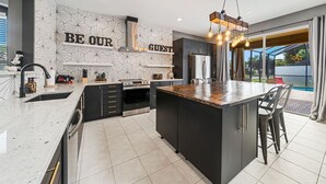 A modern kitchen with a central island, built-in appliances, and a 'BE OUR GUEST' sign on the wall. - Adventure Awaits Manor (Kissimmee)