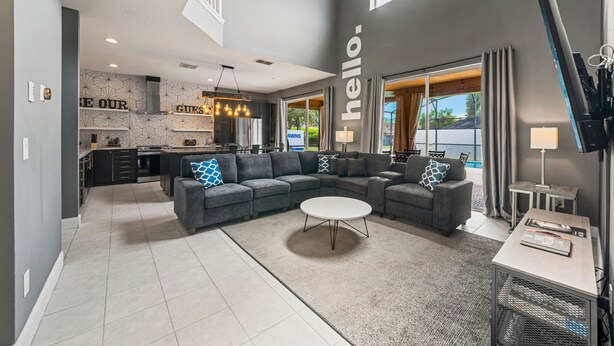 A spacious living area with a sectional sofa, a round coffee table, and a view of the kitchen in the background. - Adventure Awaits Manor (Kissimmee)
