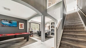 A spacious living area with a pool table, a dining area, and a staircase leading to an upper level. - Adventure Awaits Manor (Kissimmee)