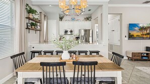 A dining area with a wooden table, black chairs, a chandelier, and a kitchen in the background. - Magical Lake View Escape! (Kissimmee)