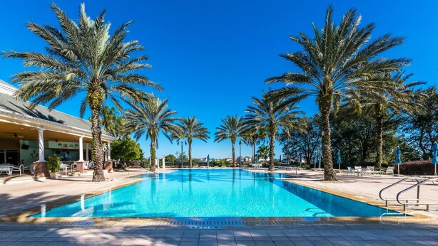 A swimming pool with palm trees and lounge chairs, surrounded by a building with columns. - Magical Lake View Escape! (Kissimmee)