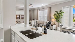A modern kitchen with a large island, a built-in sink, and a dining area with a table and chairs. - Magical Lake View Escape! (Kissimmee)