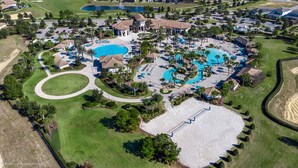 An aerial view of a resort with multiple swimming pools, a golf course, and a large sandy area.
