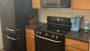 Una cocina con armarios de madera, un refrigerador negro, un microondas, una estufa y una cafetera.