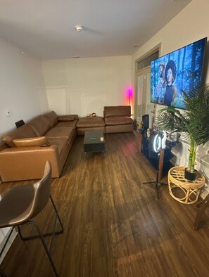 Een woonkamer met een hoekbank, een bijzettafeltje, een televisie en een potplant.