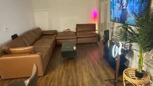 Una sala de estar con un sofá seccional, una mesita, un televisor y una planta en maceta.