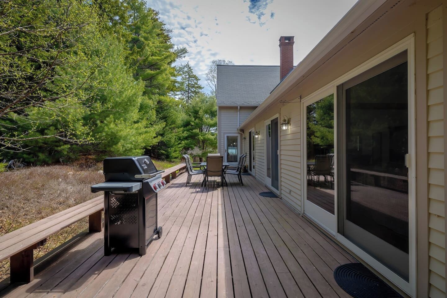 Une terrasse avec un barbecue, du mobilier d’extérieur et une maison dotée de grandes fenêtres.