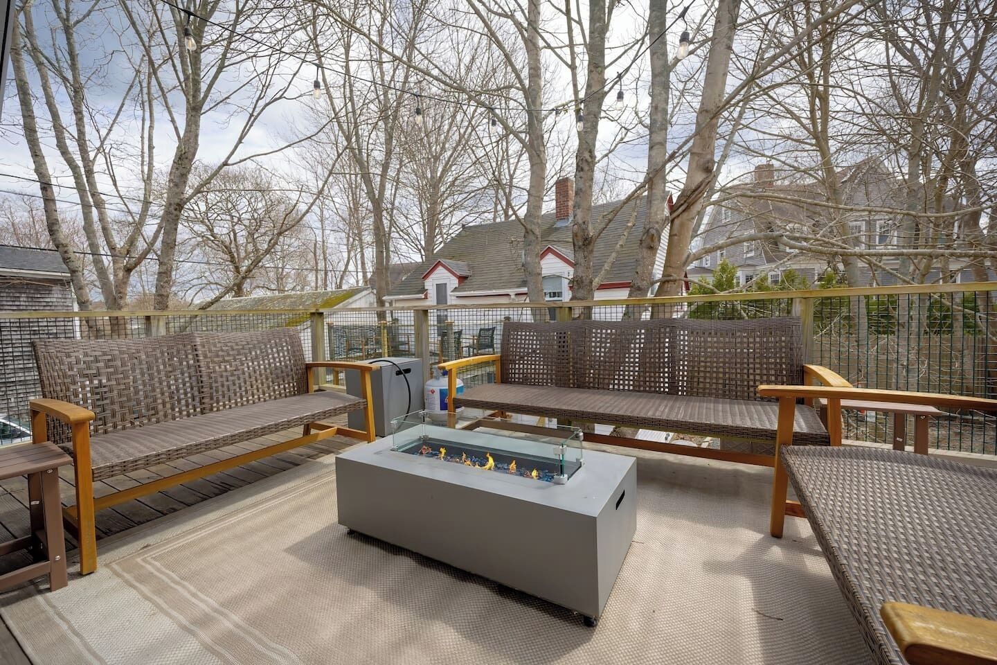 An outdoor deck with wicker furniture, a glass-top table, and a view of houses in the background.