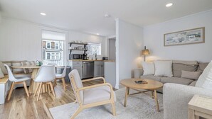 A modern apartment with a dining area, kitchen, living room, and a large window. - Renovated 3BR Home in Downtown SWH [Mariners Rest] (Southwest Harbor)