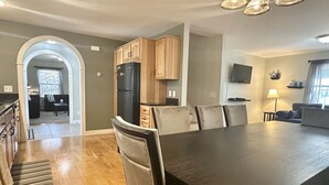 Een moderne keuken met houten kastjes, een zwarte koelkast, en een eethoek met een grote tafel en stoelen.