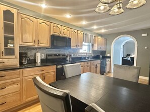 A modern kitchen with wooden cabinets, a black countertop, and a dining area with a dark table and chairs.