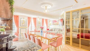A modern dining area with a glass table, pink chairs, and a chandelier. - Merveil Luxury Suite - Aboukir VII (Paris)