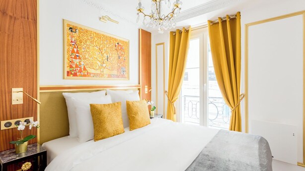 A hotel room with a large bed, a chandelier, a painting, and yellow curtains. - Merveil Luxury Suite - Aboukir VII (Paris)