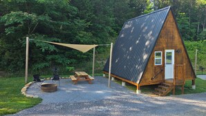 A wooden cabin with a sloped roof, a front door, and a small porch. There is a picnic table and two folding chairs outside. - Where the stars are brighter, the nights are quieter, and the Smokies feel alive (Sevierville)