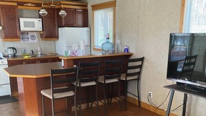 A kitchen with wooden cabinets, a microwave, a refrigerator, and a dining area with a table and chairs. - Trancequillité Lac Bitobi (Gracefield)