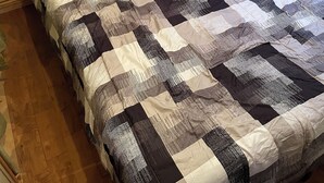 Un lit avec une couette, une prise électrique et une fenêtre avec des stores.