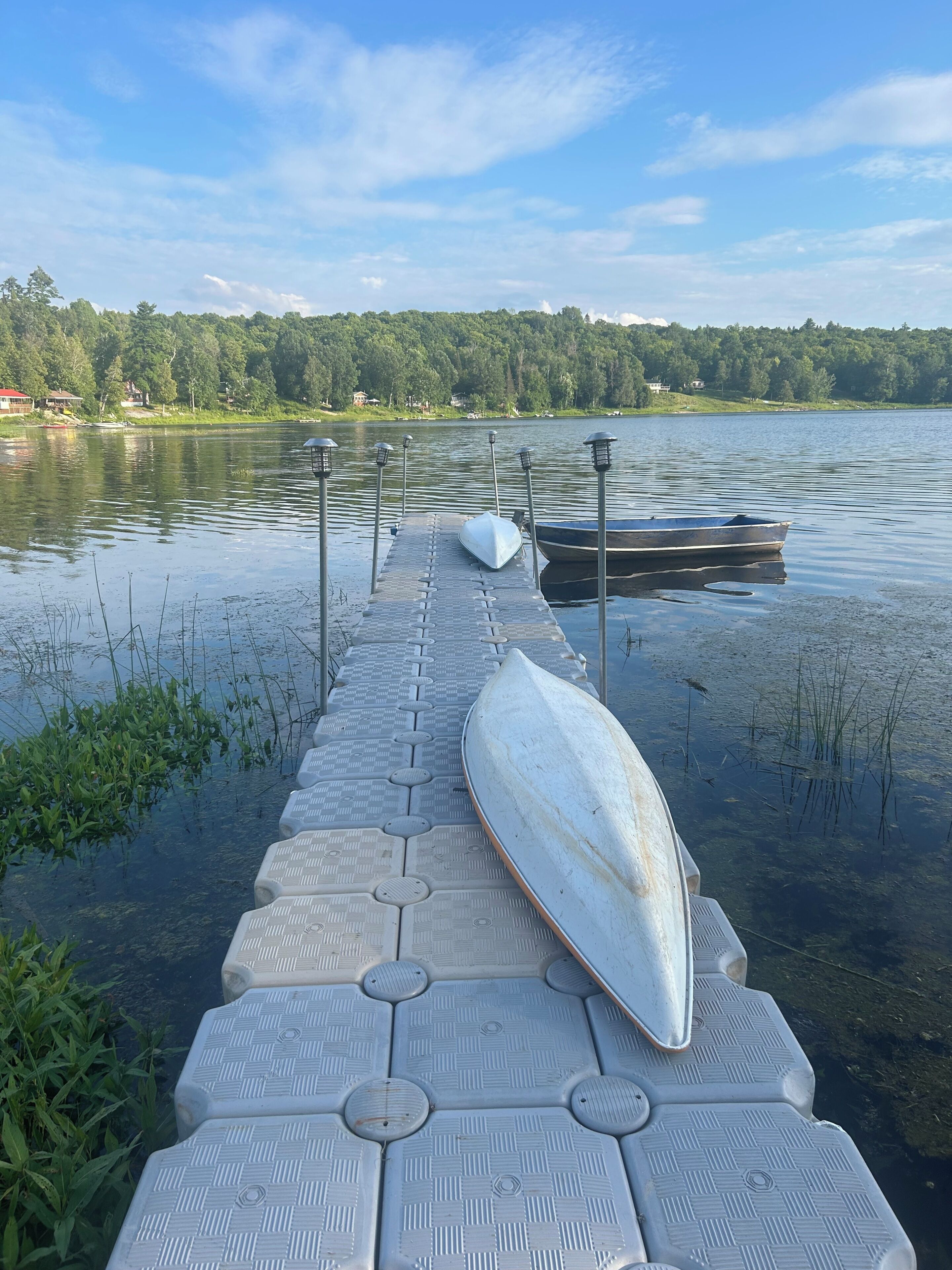 Une jetée en bois s’étendant dans un lac paisible, avec des bateaux amarrés à son extrémité.