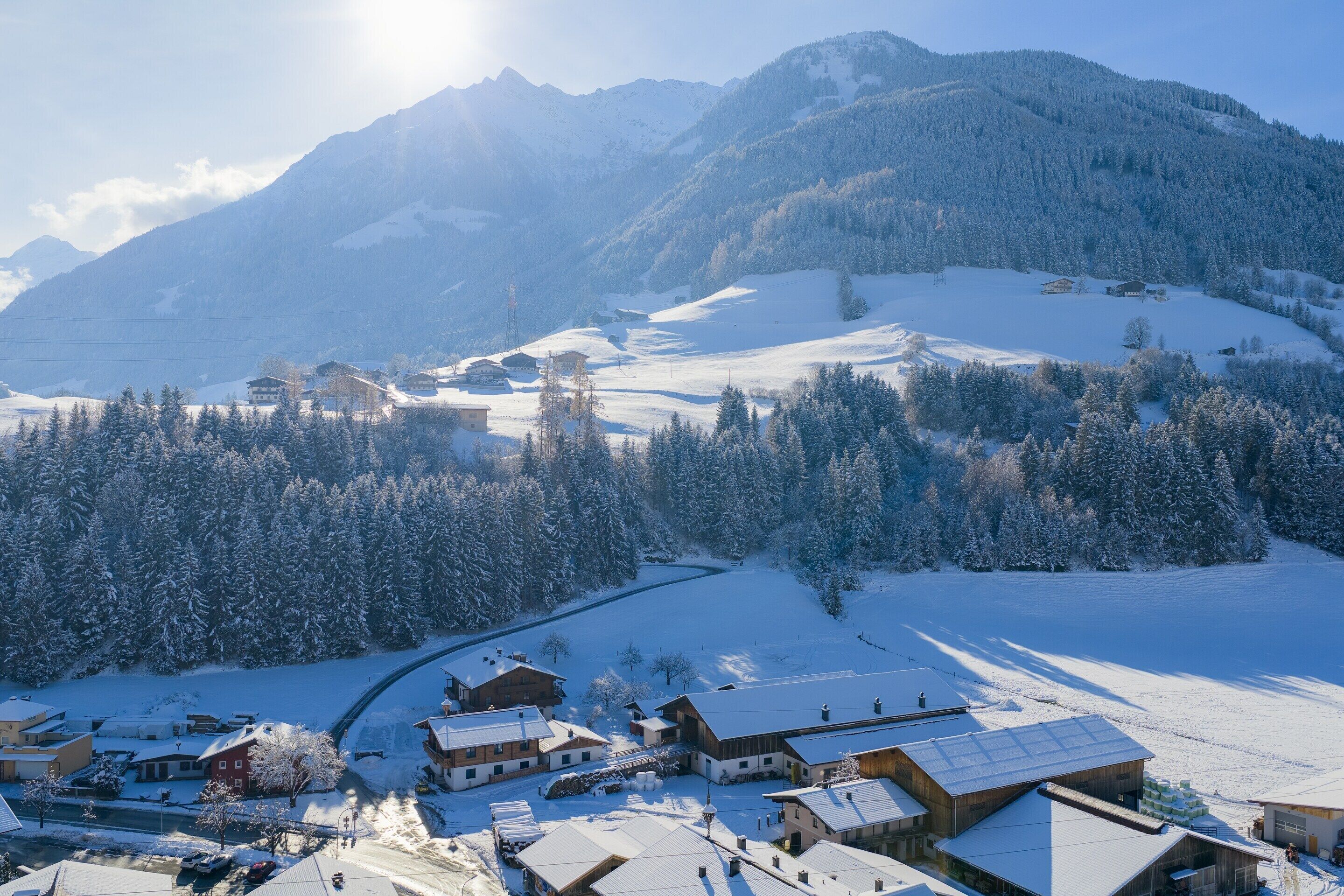 A snow-covered mountain village with traditional wooden buildings, a winding road, and a clear view of the surrounding mountains.